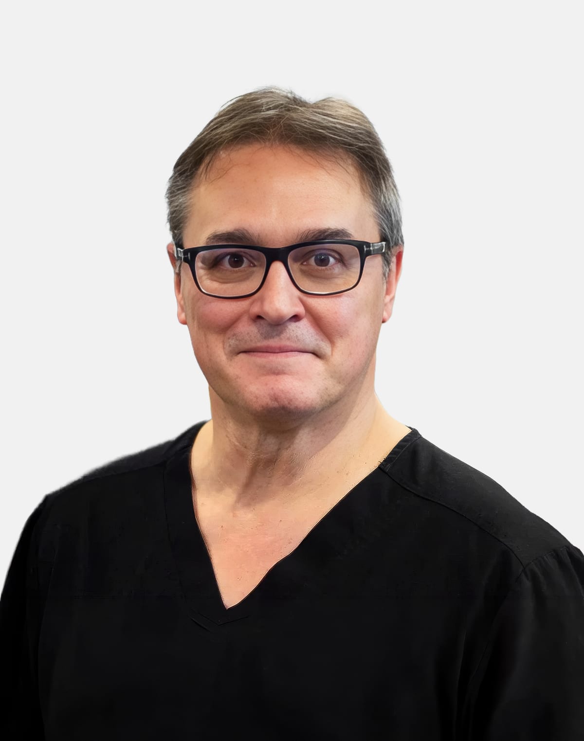 Dr. Mario Imola in black scrubs and dark-framed glasses, smiling against a light grey background